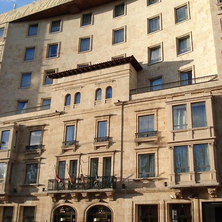 Hotel Alameda Palace Salamanca Kültér fotó The photo depicts a building with a stone facade that features a mix of architectural designs. The lower section includes several large windows framed by decorative elements, with balconies that have railings. There are also flags visible at the entr