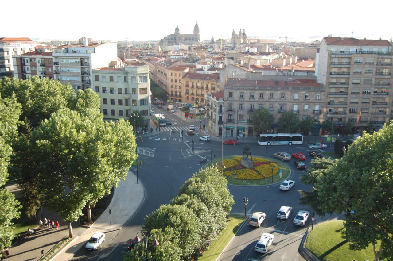 Hotel Alameda Palace Salamanca Kültér fotó The photo shows a city scene from an elevated perspective, possibly during the daytime. In the foreground, there is a roundabout with a circular flowerbed design in the center. Surrounding the roundabout, several vehicles are seen moving through the 