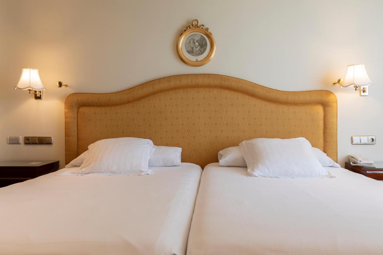 Hotel Alameda Palace Salamanca Kültér fotó The photo shows a neatly arranged hotel room with two twin beds. The beds have headboards that are upholstered in a light-colored fabric, and each bed is topped with white bedding and pillows. Above the headboard, there is a decorative round wall clo