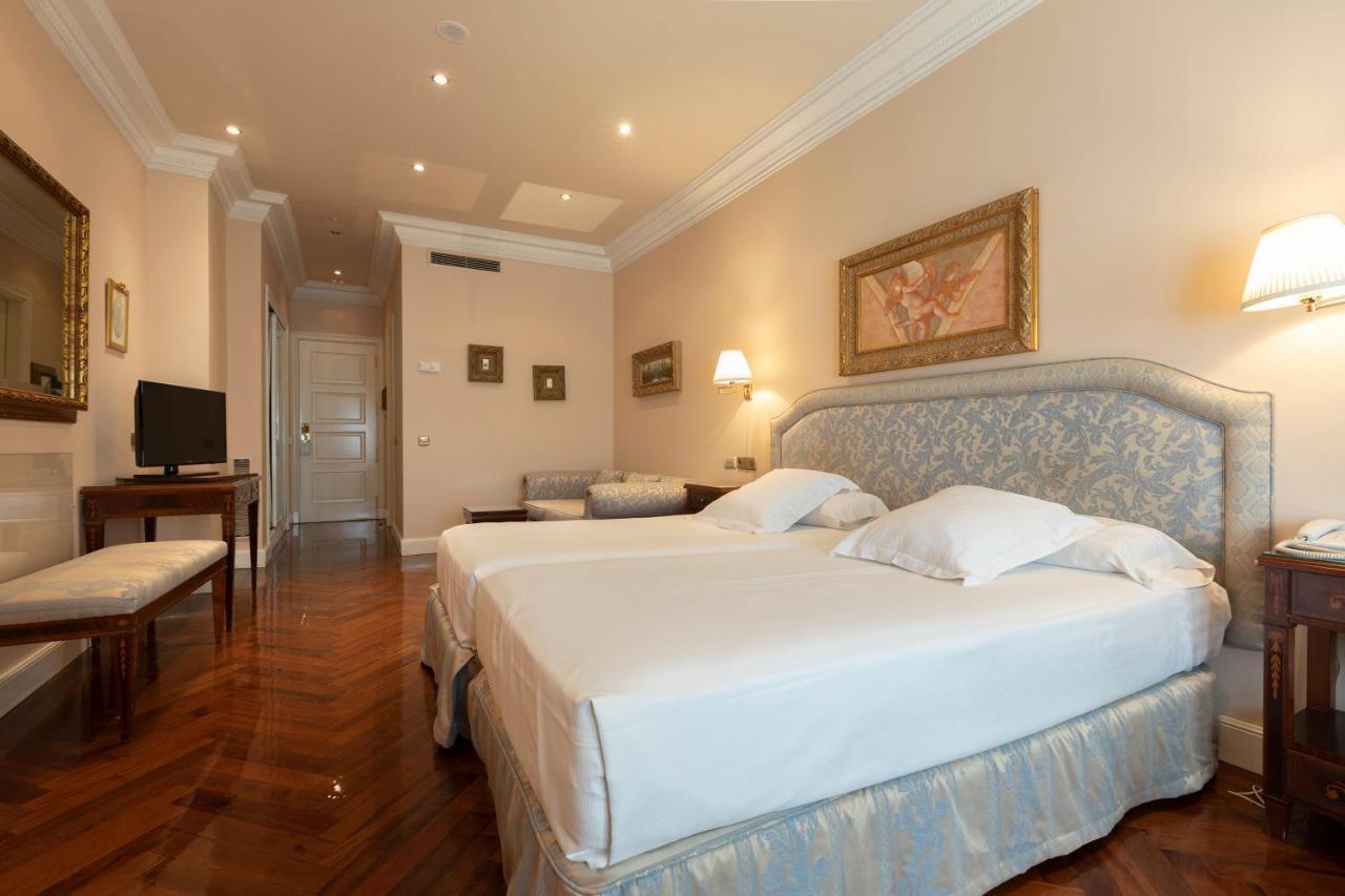Hotel Alameda Palace Salamanca Kültér fotó The photo shows an elegantly designed hotel room. It features a spacious layout with hardwood flooring and soft, warm lighting. The room includes a large bed with a light-colored headboard and white bedding, complemented by decorative pillows. Near t