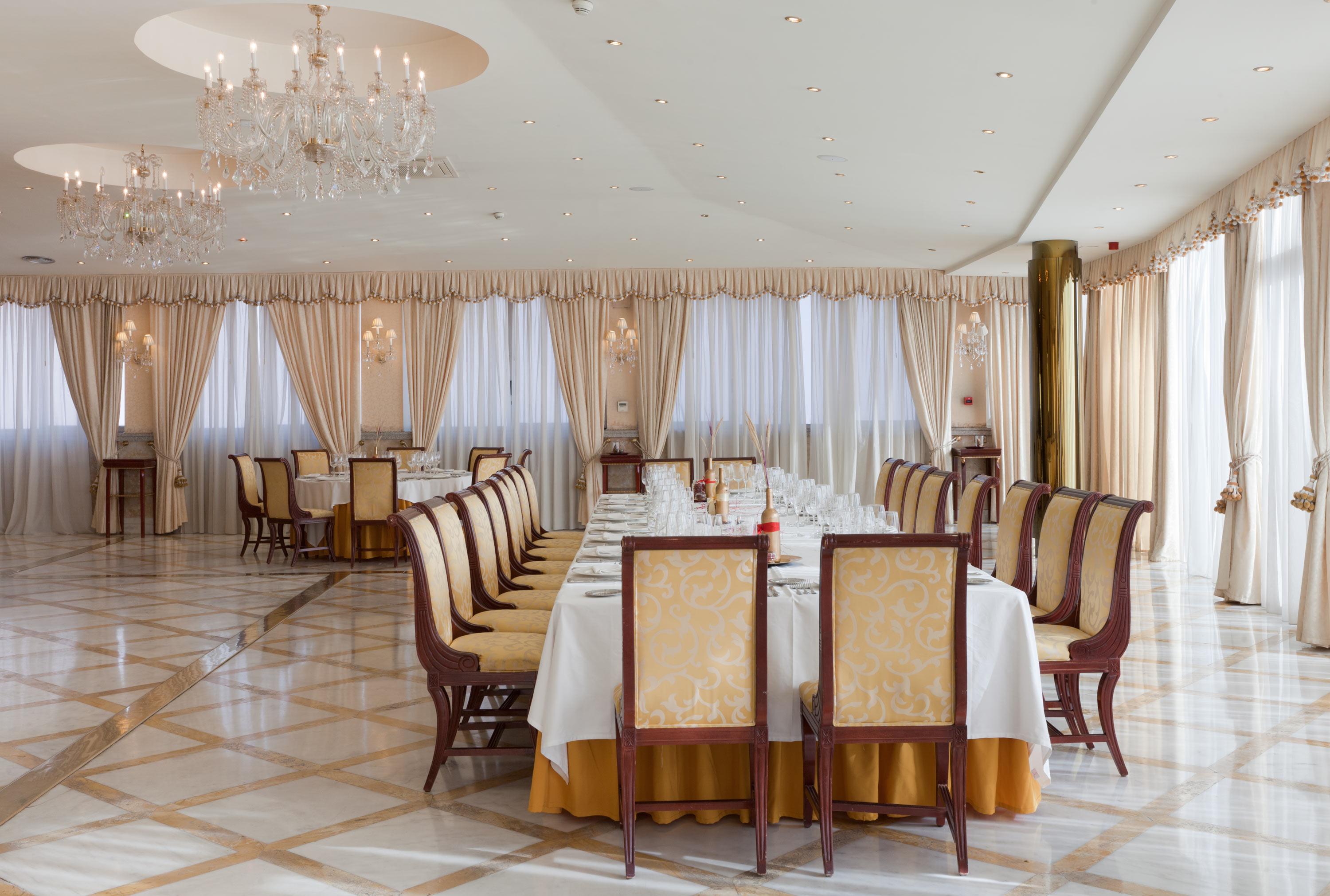 Hotel Alameda Palace Salamanca Kültér fotó The photo shows an elegant dining room with a long table set for a formal meal. The table is covered with a white tablecloth and surrounded by upholstered chairs with gold detailing. The room features large windows draped with sheer curtains, allowin