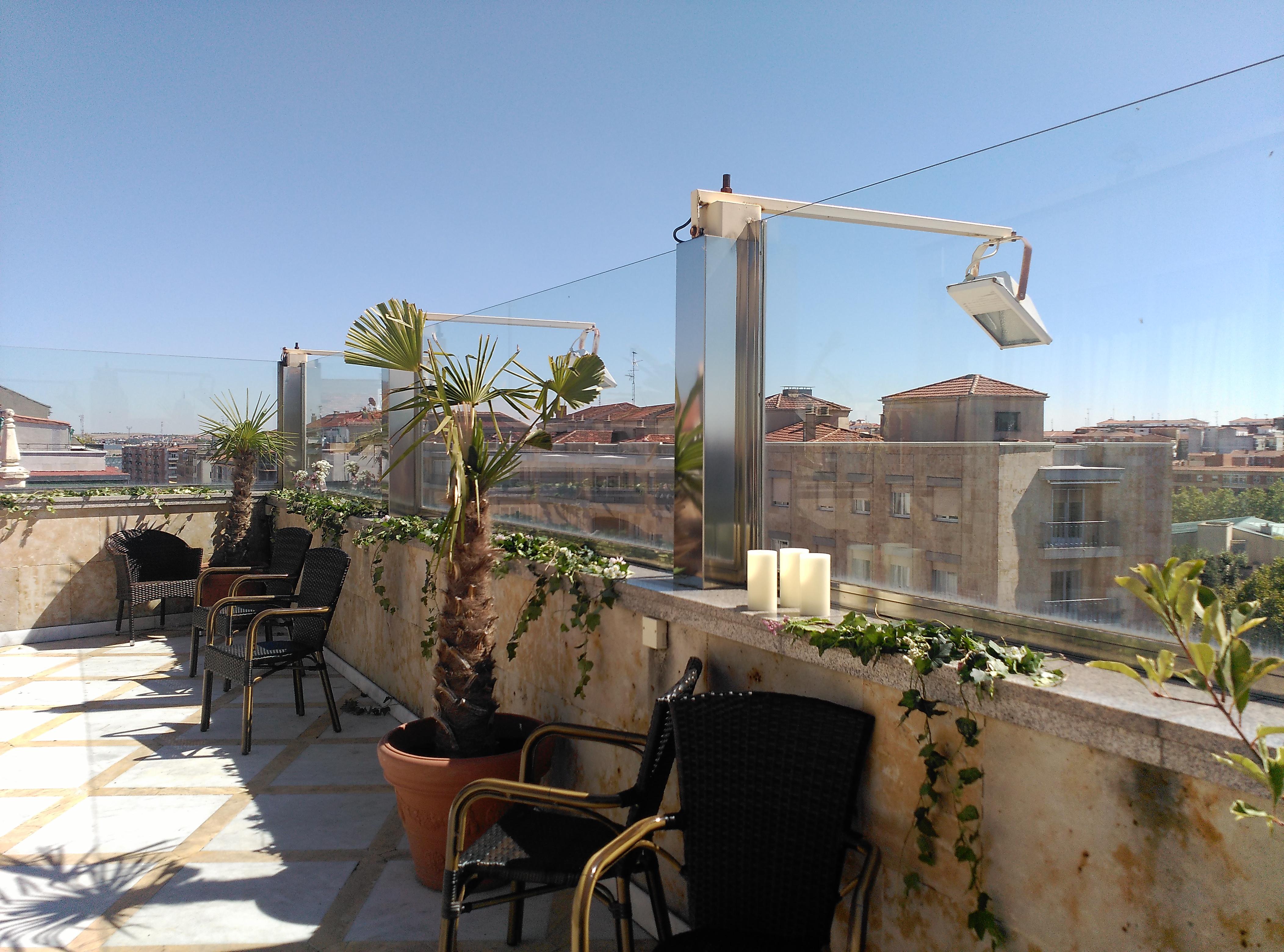 Hotel Alameda Palace Salamanca Kültér fotó The photo shows a rooftop terrace featuring a sunny environment. There are several chairs arranged on the terrace, along with potted plants, including palm-like greenery. The terrace has clear glass panels that provide a view of the surrounding build