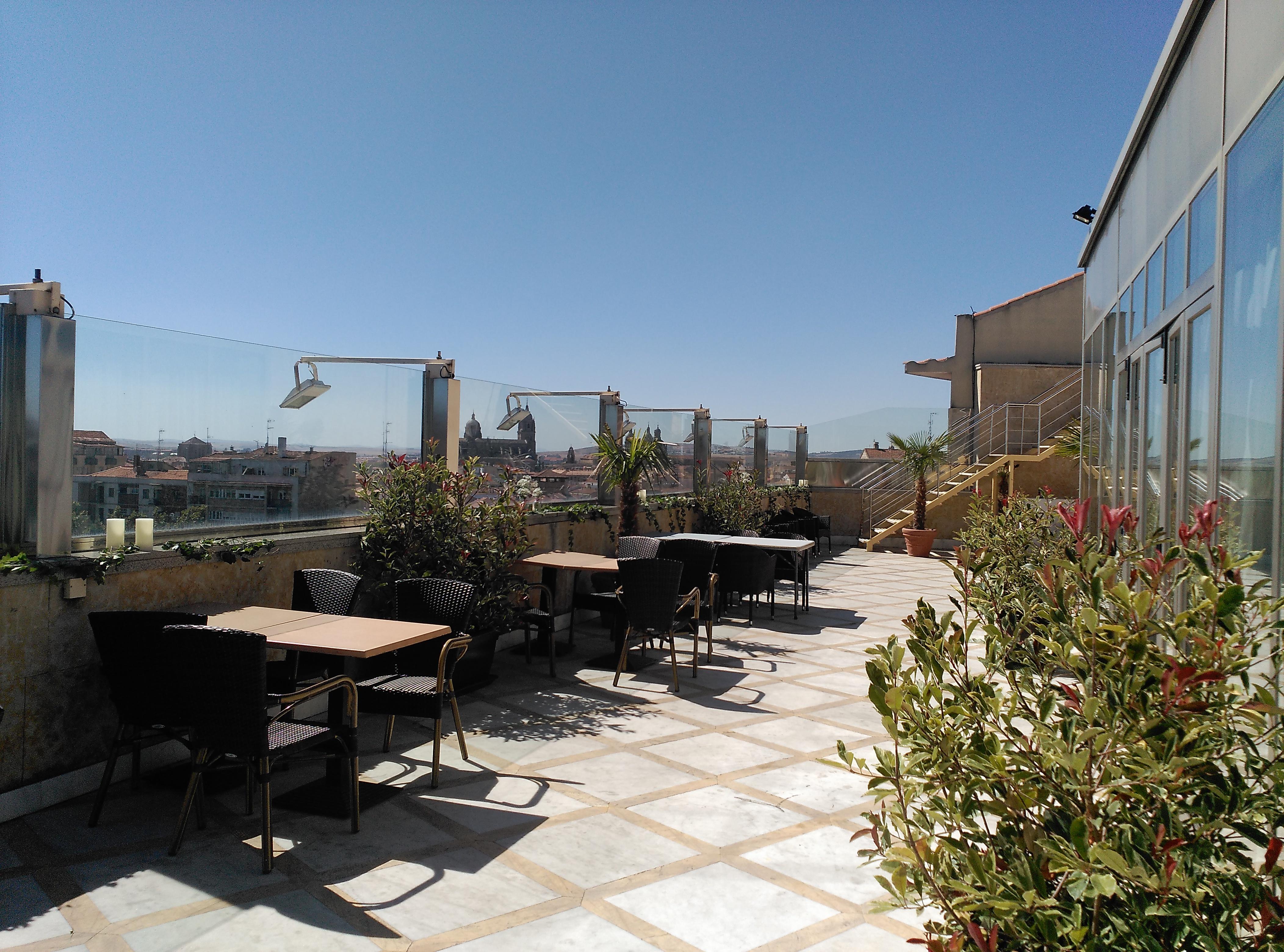 Hotel Alameda Palace Salamanca Kültér fotó The photo shows a rooftop terrace with several outdoor tables and chairs arranged in different areas. The floor appears to be tiled, and there are some plants in pots adding greenery to the space. In the background, there are cityscapes visible under