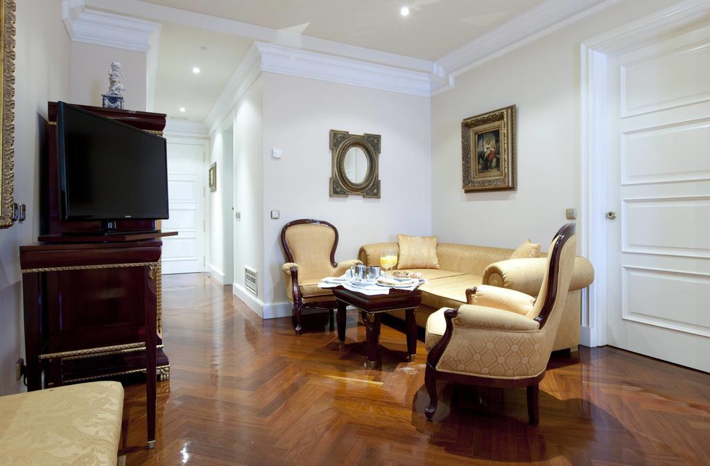 Hotel Alameda Palace Salamanca Kültér fotó The photo depicts a well-furnished living room. It features a cream-colored sofa with elegant armchairs around a dark wooden coffee table. A flat-screen television is mounted on a polished wooden unit. The floor is made of hardwood, contributing to t